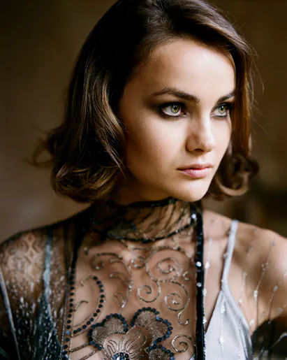 A close-up portrait of a bride with short wavy hair, dramatic smokey eye makeup, and an intricate beaded sheer dress.